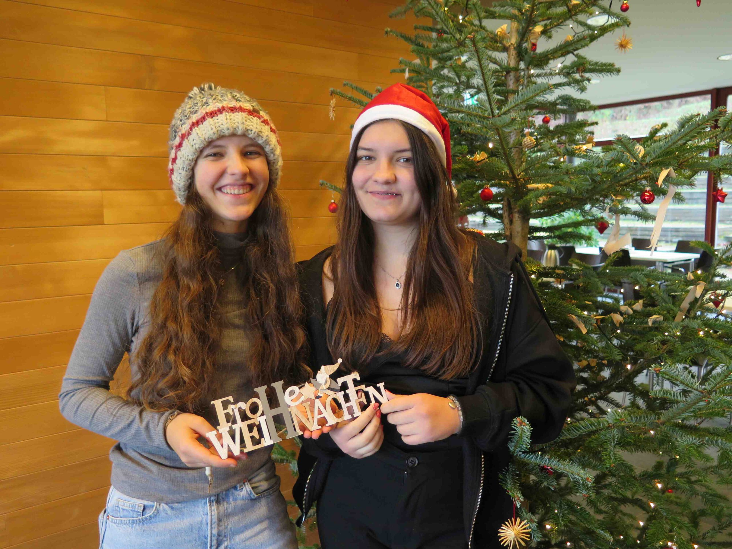 Weihnachtsgruß mit zwei WaldHaus Mitarbeiterinnen und Weihnachtsmütze vor Weihnachtsbaum